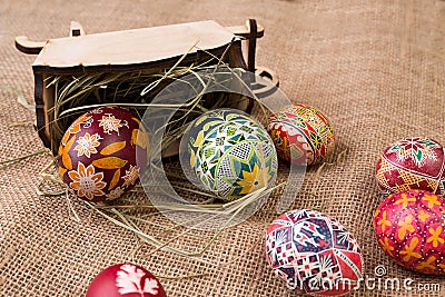 Pisanki with a wooden antique cart and hay on sackcloth. Easter eggs in ethnic style. Easter eggs on canvas. Stock Photo