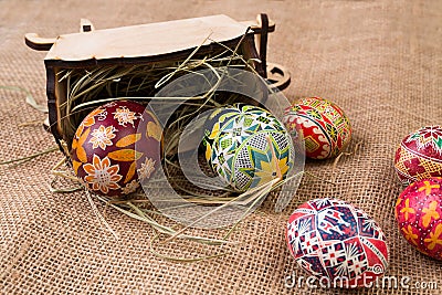 Pisanki with a wooden antique cart and hay on sackcloth. Easter eggs in ethnic style. Easter eggs on canvas. Stock Photo