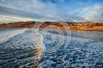 Pacific ocean at high tide. Golden hills and a beautiful cloudy sky on the background. Pismo Beach sunset, California Stock Photo