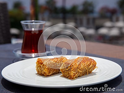 Pistachio kadayif on white plate with turkish tea on table in outdoor cafe. Stock Photo