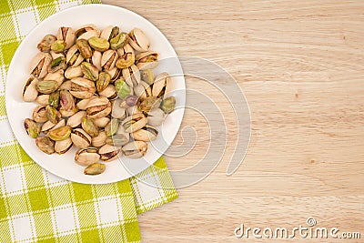 Pistachios in a white plate on a wooden table. Stock Photo