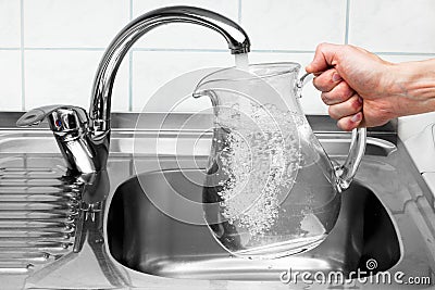 Pitcher being filled with drinking water from kitchen faucet. Stock Photo