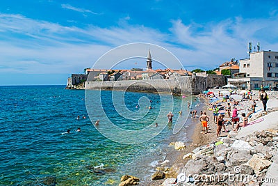 Resting people on the sandy Pizana beach against the background of the fortress walls of the citadel of the old town of Budva. Editorial Stock Photo