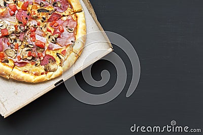 Pizza with bacon, tomatoes, salami, cheese and mushrooms in a cardboard box on dark background. Copy space. From above, Stock Photo