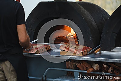 Pizza being cooked in woodfired pizza oven at outdoor party with generic unbranded pizza boxes Stock Photo