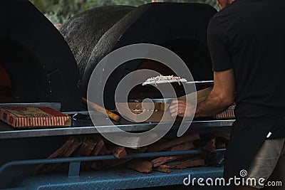 Pizza being cooked in woodfired pizza oven at outdoor party with generic unbranded pizza boxes Stock Photo