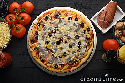 Pizza on a black background with ingredients, tomatoes, salami, mushrooms, sauce and mazzarella cheese. Italian pizza, culinary Stock Photo