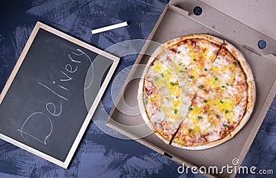 Pizza with cheese in a cardboard box and the chalkboard with the word delivery written on it Stock Photo