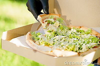 Pizza close-up in hands in medical gloves. Courier in medical mask holds pizza in hands and looks to pizza with green Stock Photo