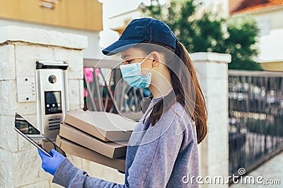 Pizza delivery girl carrying pizza boxes using the intercom at door wearing mask Stock Photo