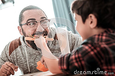 Cute generous son giving piece of pizza to his father Stock Photo