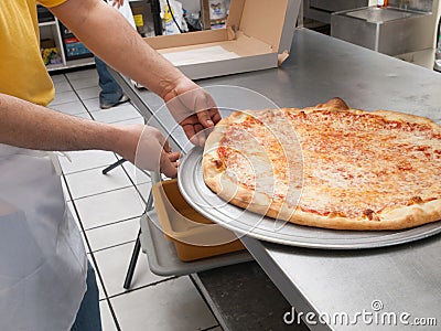 Pizza Maker removes a Fresh Pizza from the oven Stock Photo