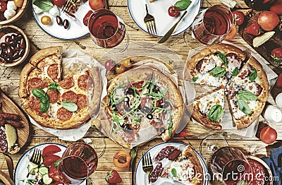 Pizza party table. Top view glasses with red wine, rustic wooden table with hot pizzas, italian appetizers, salads, cheese, fruits Stock Photo