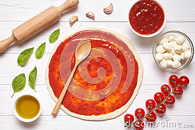 Pizza preparation. Baking ingredients on the kitchen table: rolled dough with tomatoes sauce Stock Photo