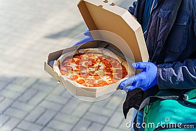 Pizza with salami and cheese in cardboard box. Safety delivery in blue medical gloves from restaurant. Quarantine for Stock Photo