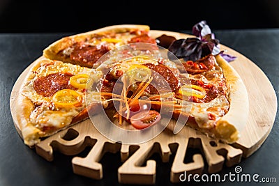 Pizza with sausage and tomatoes on a wooden round tray with a carved inscription `Pizza`. Stock Photo