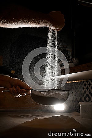 Pizzaiolo& x27;s hands sift flour through a sieve before preparing pizza in poor lighting Stock Photo