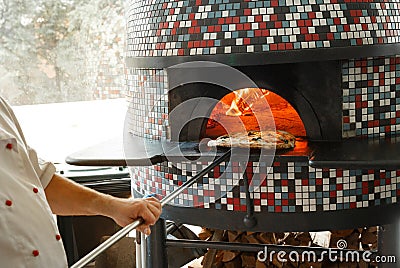 Pizzaola taking out fresh backed pizza out of traditional italian wood-fired oven Stock Photo