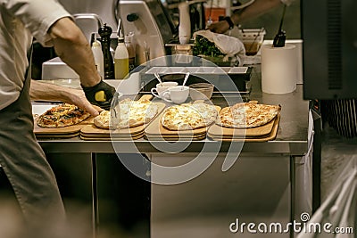 Pizzeria kitchen. Chef cook in apron and gloves cuts freshly baked pizza with roller knife Stock Photo