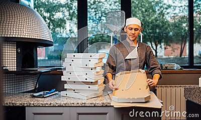Pizzeria worker building pizza packaging. Catering kitchen work. Stock Photo