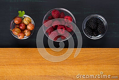 A place for inscription on a wooden surface, with three plates of black background with berries of raspberries, gooseberries, blac Stock Photo