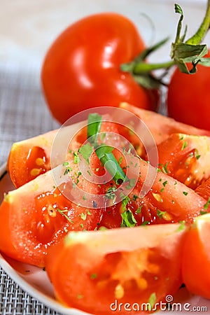 Place the sliced red tomato on a plate, sprinkle with spices and green onions Stock Photo