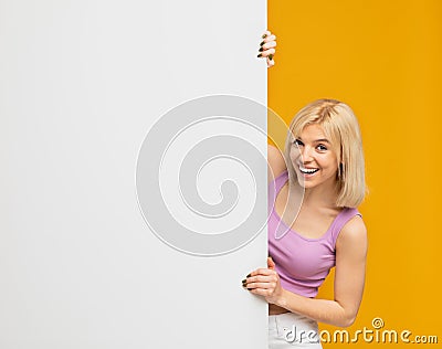 Place for your promo. Joyful woman standing behind white empty board for advertisement over yellow background Stock Photo