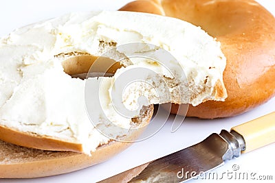 Plain bagel with knife, spread with cream cheese and bite missing, detail. Stock Photo