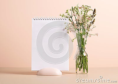 The planner's blank clean notepad stands on the table in vase with delicate green flowers. Mock up for text Stock Photo