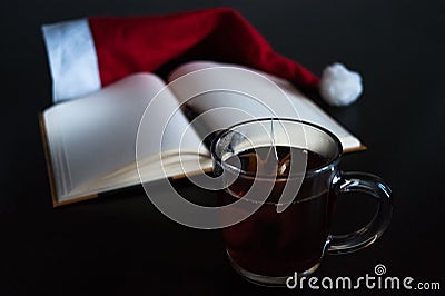 Planning future on Christmas concept: a notebook with blank pages, a black pen, Santa hat, glass mug with teabag, all on dark dini Stock Photo