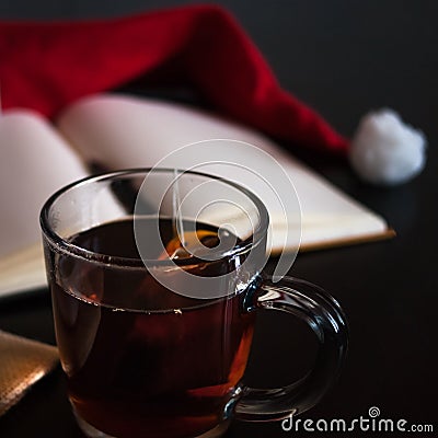 Planning future on Christmas concept: a notebook with blank pages, a black pen, Santa hat, glass mug with teabag, all on dark dini Stock Photo