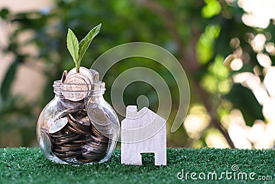 Plant growing from coins in glass jar. Wooden house model on artificial grass. Home mortgage and property investment concept Stock Photo