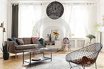 Plant next to couch and sunflowers on cabinet in white flat interior with armchair and lamp. Real photo Stock Photo