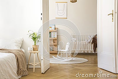 Plant on stool next to bed in white bedroom interior with rocking horse on rug and cradle Stock Photo