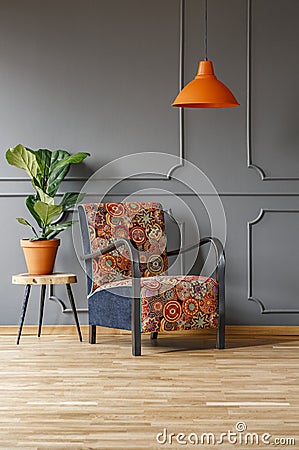 Plant on table next to patterned armchair under orange lamp in g Stock Photo