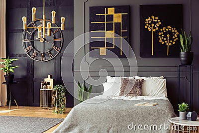 Plants and black and gold posters in grey bedroom interior with clock and bed with pillows. Real photo Stock Photo