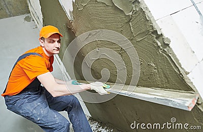 Plasterer smoothing fresh plaster on wall by straightedge trowel Stock Photo