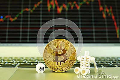 A plastic skeleton and a gold bitcoin standing on a notepad of a notebook computer with a stock graph in the background Editorial Stock Photo