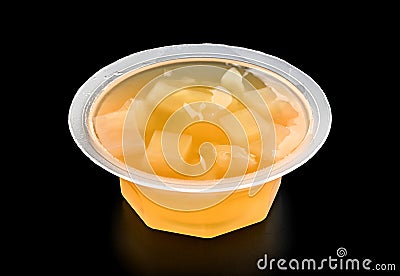 Plastic bowl with orange jelly and pieces of fruit close-up isolated on black background Stock Photo