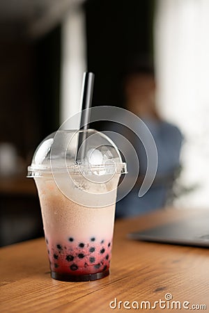 Plastic cup of fresh bubble drinks on wooden table in cafe over male client background Stock Photo