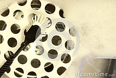 A plastic dish-brush lies on top of a plate in a sink Stock Photo