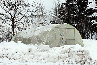 Plastic greenhouse with wooden doors surrounded with snow Stock Photo
