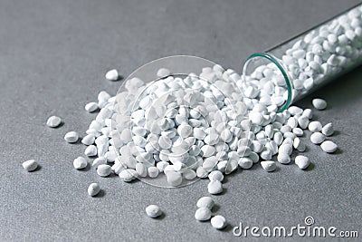 Plastic pellets. White Colorant for plastics, in test-tube against a silvery metallic background. Stock Photo