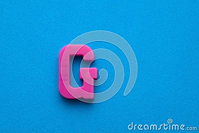 Alphabet letter G - Pink plastic piece on blue foamy background Stock Photo