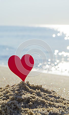 Plastic stick in shape of red heart in sand on sandy beach of sea shore Stock Photo