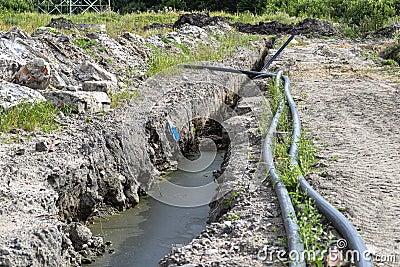 Plastic water pipe lying along the ditch with high groundwater, water connection in the housing estate. Stock Photo