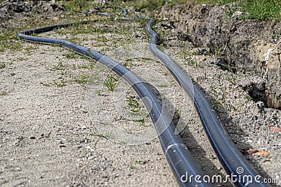 Plastic water pipe lying along the ditch with high groundwater, water connection in the housing estate. Stock Photo