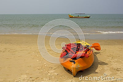 Plastic yellow-orange kayak with paddles and red life vests, stands on a sandy beach against the background of the sea and a large Stock Photo