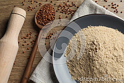 Plate with buckwheat flour, grains and rolling pin on wooden table Stock Photo