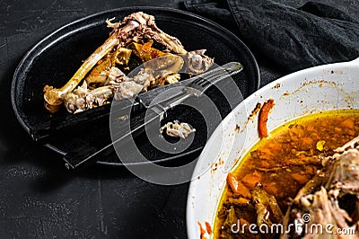 A plate of chicken bones and a chicken skeleton in a baking dish. Leftovers from dinner. Black background. Top view Stock Photo